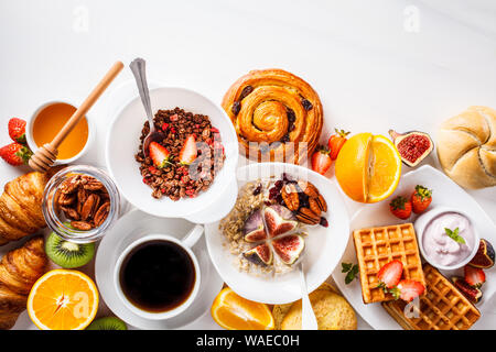 Frühstückstisch mit Haferflocken, Müsli, Waffeln, Croissants und Obst. Weißer Hintergrund. Stockfoto