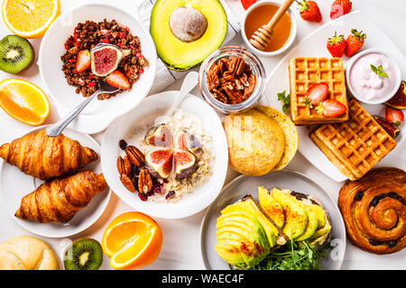 Frühstückstisch mit Avocado Toast, Müsli, Waffeln, Croissants auf einem weißen Hintergrund. Stockfoto