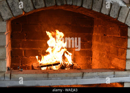 Feuer Holz Brennen im Ofen. Feuer in einem Steinofen. Der Herd, auf der Straße. Vorbereitung für die Zubereitung des Abendessens. Rauch vom Feuer. Brick Wall Stockfoto