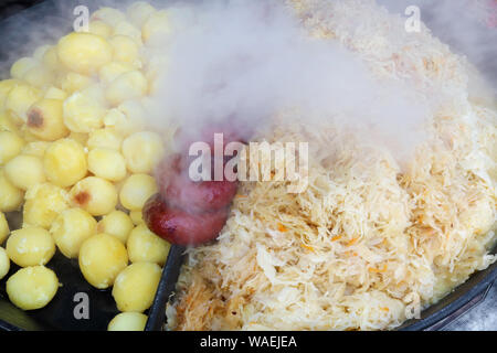 Schnelle Street - Nahrung - geräuchertes Schweinefleisch Würstchen, gebratenen Kartoffeln und Kohl in großen eisernen Schwarze Pfanne. Snapshot stil Bild Stockfoto