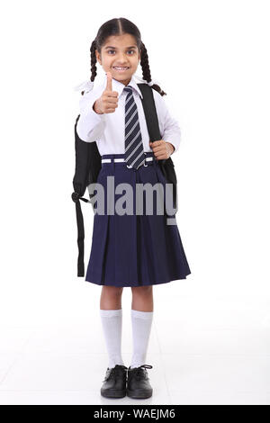 Schulmädchen stehend mit Rucksack und zeigt Daumen hoch Zeichen Stockfoto