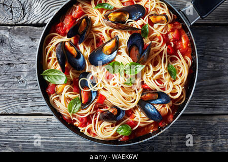 Nahaufnahme der Pasta mit Miesmuscheln in einer würzigen Tomatensauce in einer Pfanne auf einem alten rustikalen Holztisch, horizontale Ansicht von oben, flatlay, Makro Stockfoto