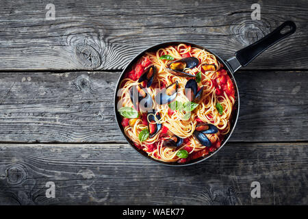 Pasta mit Miesmuscheln in einer würzigen Tomatensauce in einer Pfanne auf einem alten rustikalen Holztisch, horizontale Ansicht von oben, flatlay, kopieren Raum Stockfoto