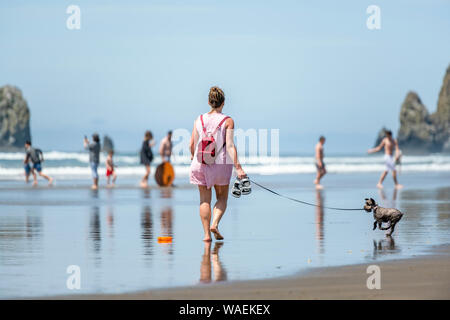 Elegante Frau in Sonnenbrille mit einem kleinen Rucksack Barfuß-Wanderungen mit einer Miniatur terrier an der Leine entlang des Pazifischen Ozeans im Nordwesten, dabei auf Stockfoto