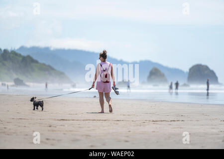 Elegante Frau in Sonnenbrille mit einem kleinen Rucksack Barfuß-Wanderungen mit einer Miniatur terrier an der Leine entlang des Pazifischen Ozeans im Nordwesten, dabei auf Stockfoto