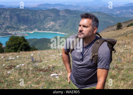 Wanderer steigt den Hügel, mit dem Rucksack auf den Schultern. Im Hintergrund eine schöne Landschaft von See und die Berge. An einem Sommertag in Italien. Ha Stockfoto