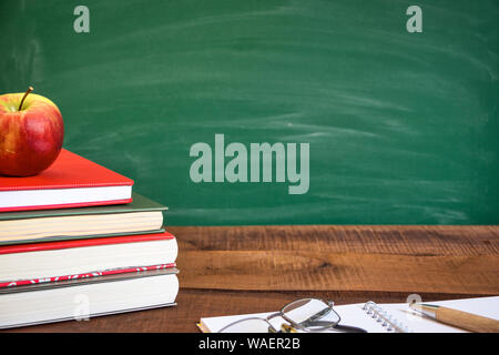 Bücher und Apple auf holztisch vor der Schule Schiefertafel. Zurück zum Konzept der Schule. Kopieren Raum auf der rechten Seite. Stockfoto