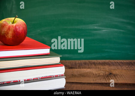 Bücher und Apple auf holztisch vor der Schule Schiefertafel. Zurück zum Konzept der Schule. Kopieren Raum auf der rechten Seite. Stockfoto