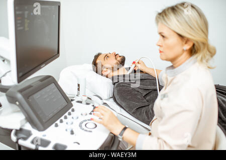 Weibliche Arzt führt eine Ultraschalluntersuchung der Schilddrüse Männer in der Arztpraxis. Konzept der Ultraschalldiagnostik der männlichen Gesundheit Stockfoto