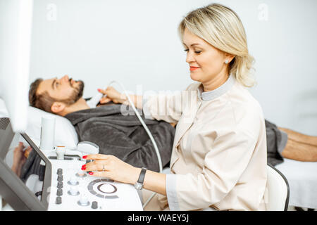 Weibliche Arzt führt eine Ultraschalluntersuchung der Schilddrüse Männer in der Arztpraxis. Konzept der Ultraschalldiagnostik der männlichen Gesundheit Stockfoto