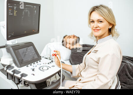 Weibliche Arzt führt eine Ultraschalluntersuchung der Schilddrüse Männer in der Arztpraxis. Konzept der Ultraschalldiagnostik der männlichen Gesundheit Stockfoto