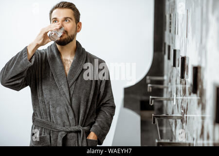 Schöner Mann im Bademantel trinken Mineralwasser Thermalwasser an der Pumpe - Zimmer und ruhen auf dem Luxus Resort Stockfoto