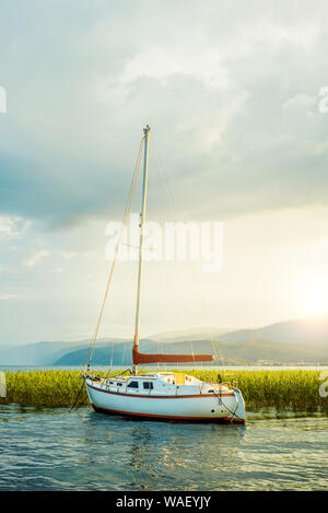 In Mazedonien. Ohrid. Weißes Segelboot auf Ohrid-see neben Schilf in den Sonnenuntergang. Vertikale Foto. Stockfoto