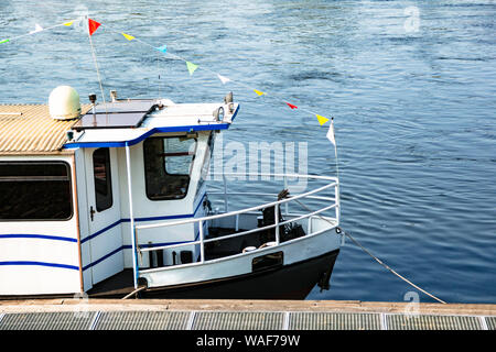 Sightseeing-Boot am hölzernen Pier am Fluss festgemacht Stockfoto