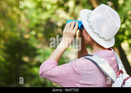 Ansicht der Rückseite des reife Frau in hat ständigen draußen im Park und der Blick durch ein Fernglas auf schöne Aussicht während Wandern Stockfoto