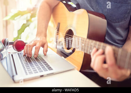Musiker, der Akustikgitarre spielt und Musik am Computer aufnimmt oder aus dem Online-Unterricht lernt Stockfoto
