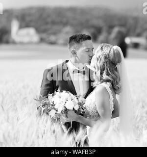 Braut und Bräutigam küssen und zärtlich umarmen in Weizen Feld irgendwo in der Landschaft in slowenischer Sprache. Kaukasische gerne romantische junge Paar feiern. Stockfoto