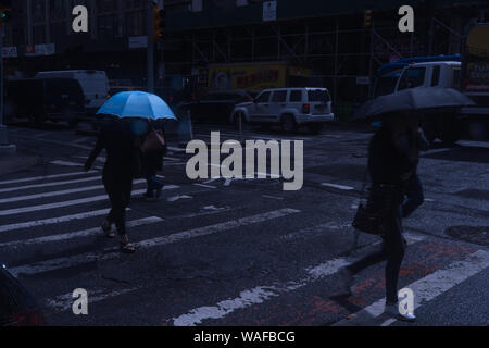 New York City, ca. 2019: Nacht über Manhattan crosswalk während der Rush Hour im Regen. Blau Schirmständer aus der Finsternis unter bunten Mo Stockfoto