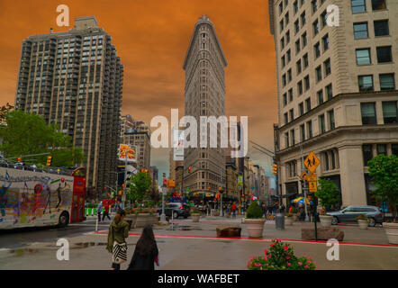 New York City, ca. 2019: Dramatische orange Sonnenuntergang Himmel über das Flatiron Building in Manhattan während der abendlichen Hauptverkehrszeit pendeln. Seltsame Dinge Stockfoto