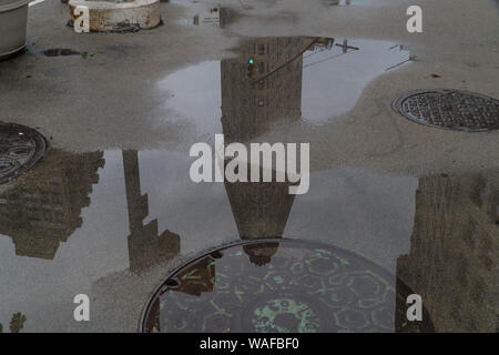 Menschen gehen während des morgendlichen Berufsverkehrs entlang zu Fuß mit generischen Gebäude Reflexion Skyline in Regen Pfütze zu stürmischen Himmel suchen in Wasser Stockfoto