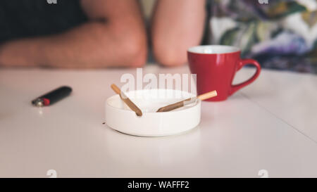 Zwei medizinisches Marihuana Joins werden in den Aschenbecher, eine Tasse Kaffee und Feuerzeug in der Nähe. Das Rauchen von Marihuana gemeinsamen Zuhause. Cannabis ist ein Konzept von pflanzlichen Med Stockfoto