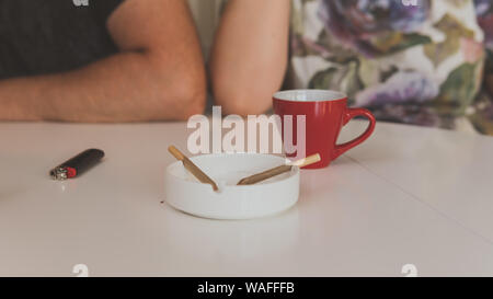 Zwei medizinisches Marihuana Joins werden in den Aschenbecher, eine Tasse Kaffee und Feuerzeug in der Nähe. Das Rauchen von Marihuana gemeinsamen Zuhause. Cannabis ist ein Konzept von pflanzlichen Med Stockfoto