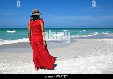 Schöne Frau in einem roten Sommer Kleid und Hut stehen auf dem Strand Stockfoto