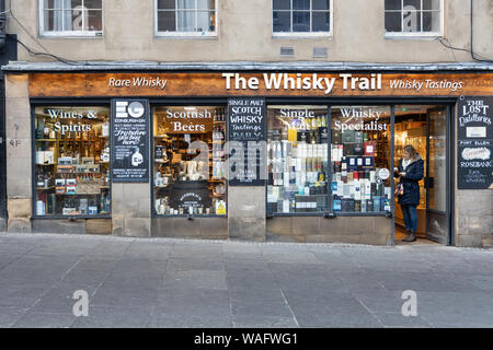 Shop vor der Whisky Trail angezeigte Flaschen Whisky mit einer Dame am Eingang. High Street, Royal Mile, Edinburgh Schottland Großbritannien Stockfoto