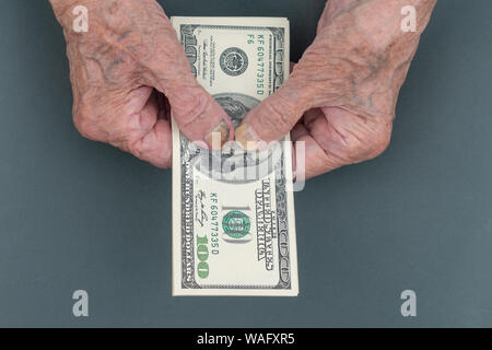 Armen alten Frau zählt einige amerikanische Dollar in der Hand. faltigen Hände einer alten Frau. Zählen von Geld, Wirtschaft Konzept, das Geld zu teilen. Thri Stockfoto