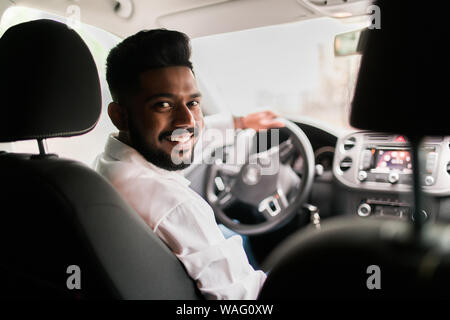 Rückansicht, junger Mann mit seinem Auto, Blick in die Kamera Stockfoto