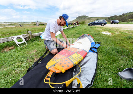 Urlaub waxing Surf Board im Freien am Strand Surfer. Der Mensch ist das Entfernen oder Anwendung von Wachs auf Surfboard shortboard auf Urlaub. Spuren von Wachs sind gegenüber Stockfoto