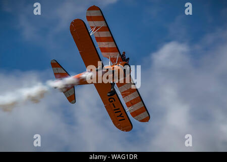 Orange Boeing Wingwalker Aerobatic Doppeldecker mit weißer Rauch und eine Frau auf dem Flügel einer Ebene Stockfoto