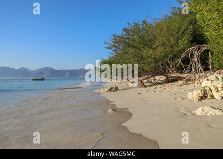 Meer Wasser wäscht die feinen gelben Sand Strand auf Gili Meno Insel in Indonesien. Mooring Yacht auf See nicht weit von der Küste. Tropische Sträucher und Bäume. Stockfoto