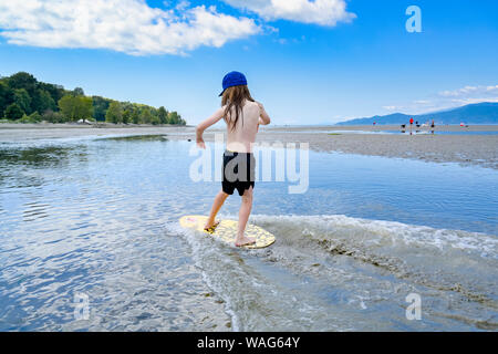 Die jungen langhaarigen Jungen skimboarding, Spanische Banken, English Bay, Vancouver, British Columbia, Kanada Stockfoto