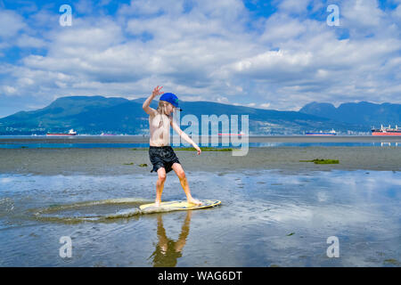 Die jungen langhaarigen Jungen skimboarding, Spanische Banken, English Bay, Vancouver, British Columbia, Kanada Stockfoto