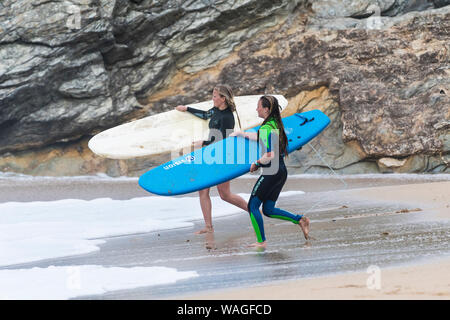 Junge weibliche Surfer Durchführung ihrer surboards, wie Sie in das Meer bei Fistral in Newquay in Cornwall. Stockfoto