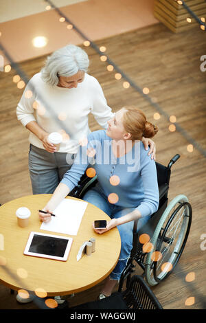 Ältere Mutter Kaffee zu trinken und zu reden ihre behinderte Tochter im Rollstuhl, während Sie ein Dokument füllen Sie haben ein Treffen im Cafe Stockfoto