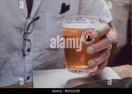 London, Großbritannien - 29 Juli, 2019: Mann hält ein Glas Camden Town Brauerei Bier. Camden Town ist eine in London ansässige Brauerei im Jahr 2010 lag gegründet Stockfoto