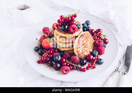 Quark Pfannkuchen serviert mit viel frische Beeren auf weißem Hintergrund. Gourmet Frühstück - Hüttenkäse syrniki, Quark Krapfen mit raspberr Stockfoto