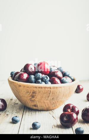 Schüssel von reifen Kirschen und Heidelbeeren. Große Sammlung von frisch gepflückte reife Beeren auf Holz- Hintergrund. Kopieren Sie Platz. Stockfoto