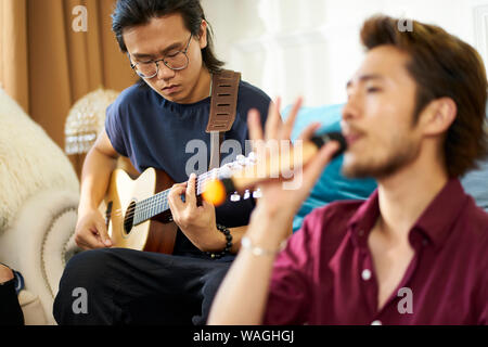 Jungen asiatischen erwachsene Männer Rock Band Mitglieder Proben singen die Musikinstrumente im Wohnzimmer eines Hauses Stockfoto