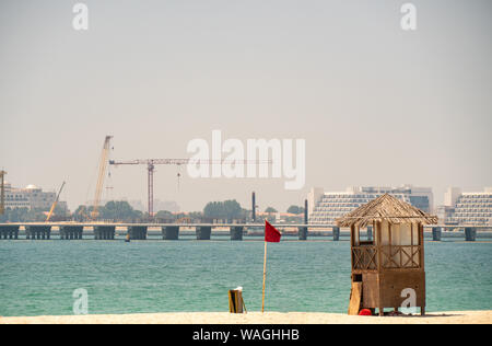 Blick auf einen leeren Strand mit einer roten Fahne und Life Guard Post. Dubai Strand mit einem Kran im Hintergrund Stockfoto