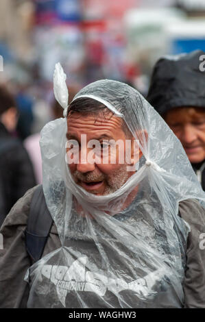 Edinburgh, Schottland, Großbritannien. 20. August 2019. Ein Mann nimmt die Abdeckung vom starken Regen auf der Royal Mile in Edinburgh Fringe Festival. Credit: Skully/Alamy leben Nachrichten Stockfoto