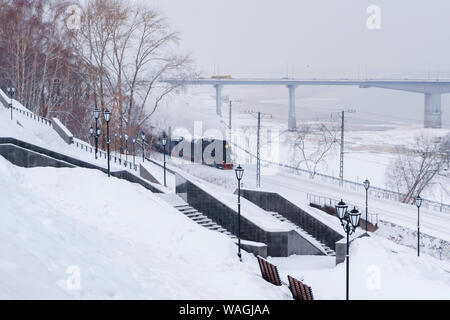 Winter verschneite Landschaft mit Dampflokomotive in Bewegung entlang der Ufer mit Automobil Bridge im Hintergrund Stockfoto