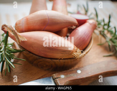 Nahaufnahme der Schalotten in eine hölzerne Schüssel mit frischem Rosmarin auf Schneidebrett Stockfoto