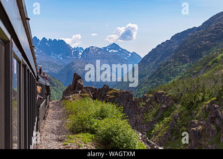 Eine Schmalspurbahn entlang White Pass Canyon in Richtung skagway Alaska mit Bergspitzen im Hintergrund Stockfoto