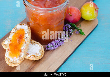 Hausgemachtes Pflaumenmus in Glas Glas mit Toast und Pflaumen auf Holztisch und blauem Hintergrund. Stockfoto