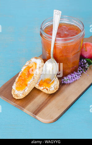 Hausgemachtes Pflaumenmus in Glas Glas auf Holztisch und blauem Hintergrund. Stockfoto