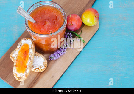 Hausgemachtes Pflaumenmus in Glas Glas mit Toast und Pflaumen auf Holztisch und blauem Hintergrund. Stockfoto