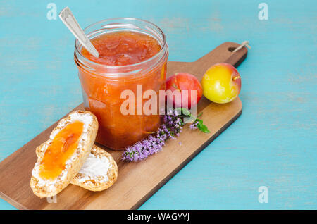 Hausgemachtes Pflaumenmus in Glas Glas mit Toast und Pflaumen auf Holztisch und blauem Hintergrund. Stockfoto